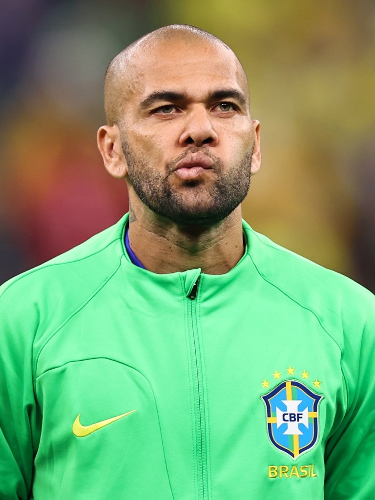 Athlete in a green sports jacket with the Brazil national football team emblem, looking serious with pursed lips.